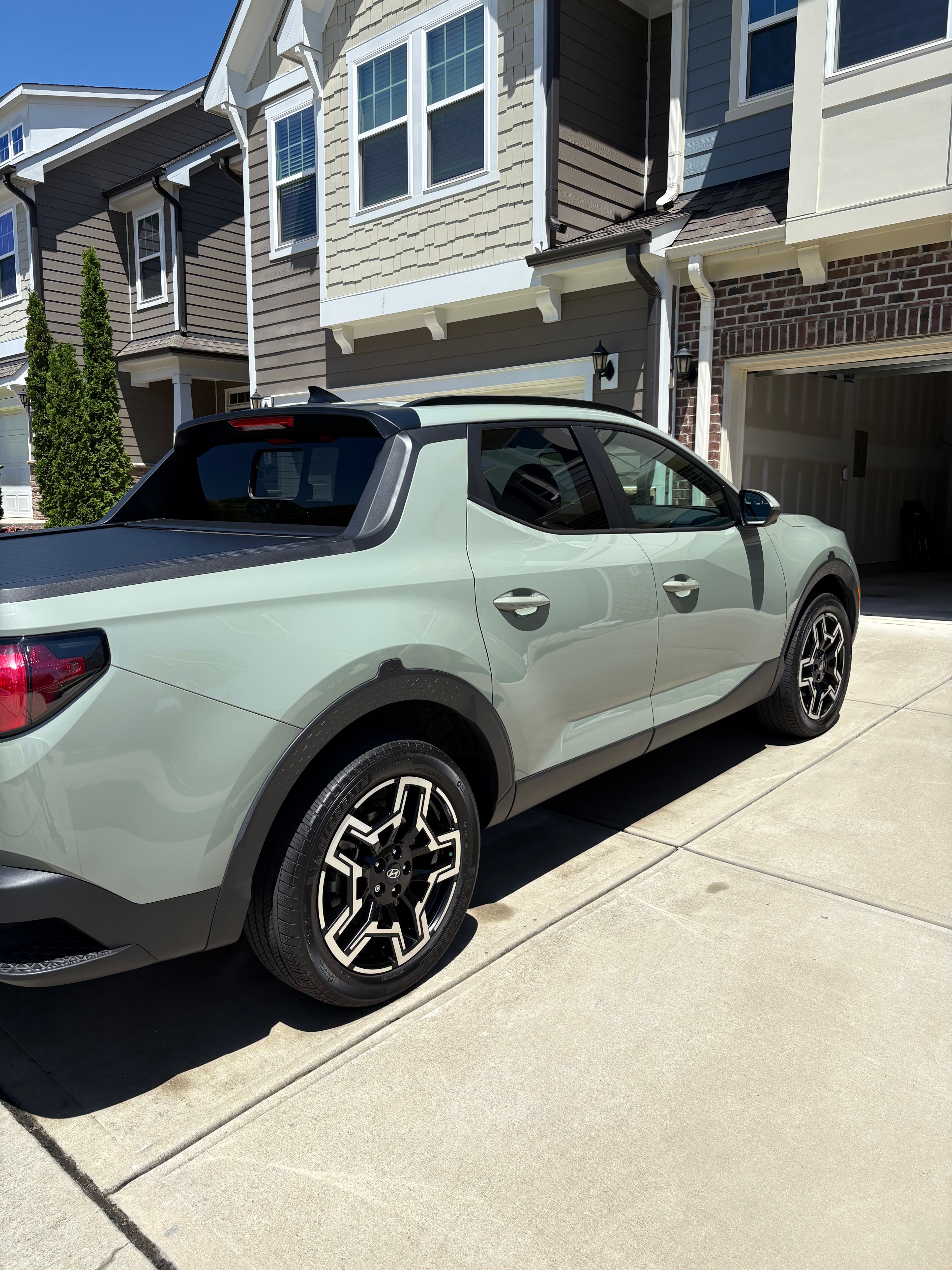 Sage green Hyundai Santa Cruz parked in a sunny driveway outside a modern townhouse.