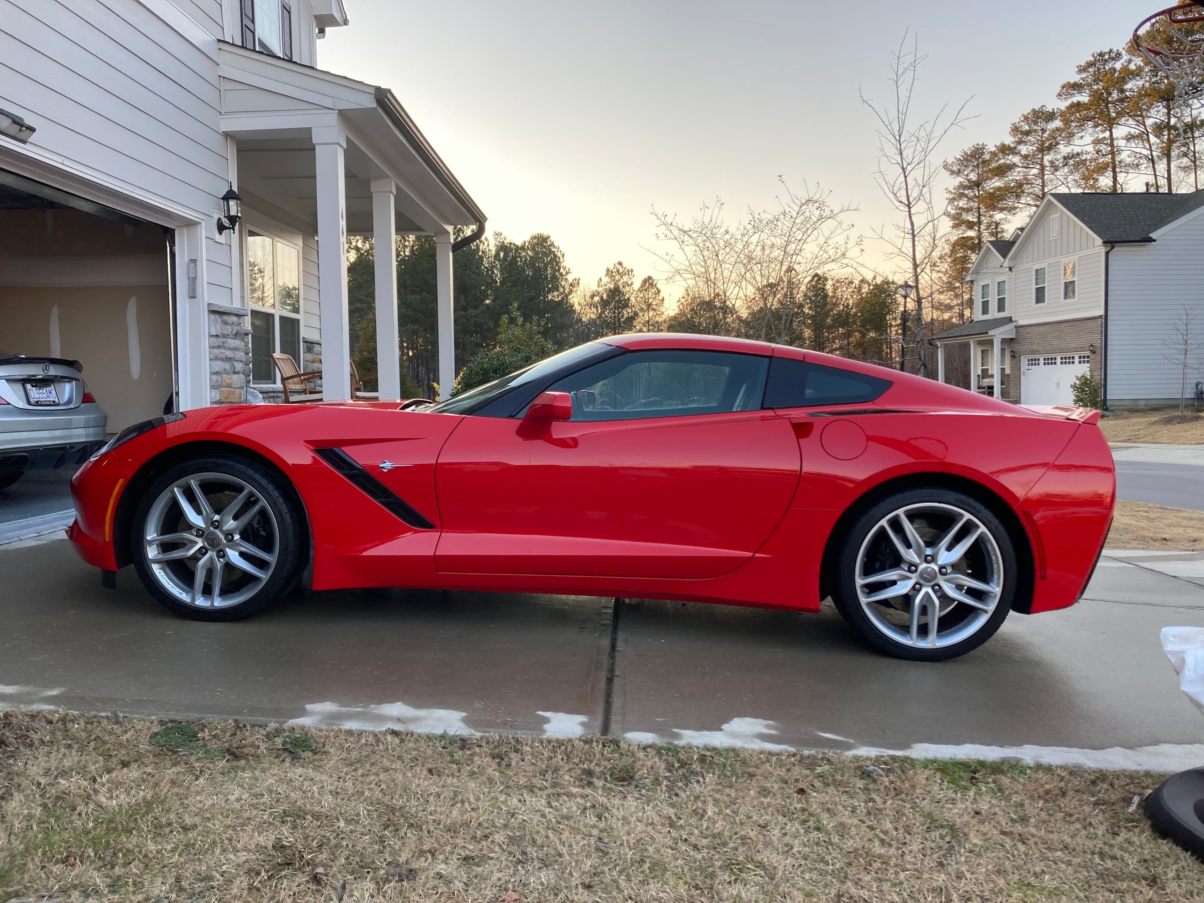 Sleek red Chevrolet Corvette parked on a concrete driveway in front of a house.