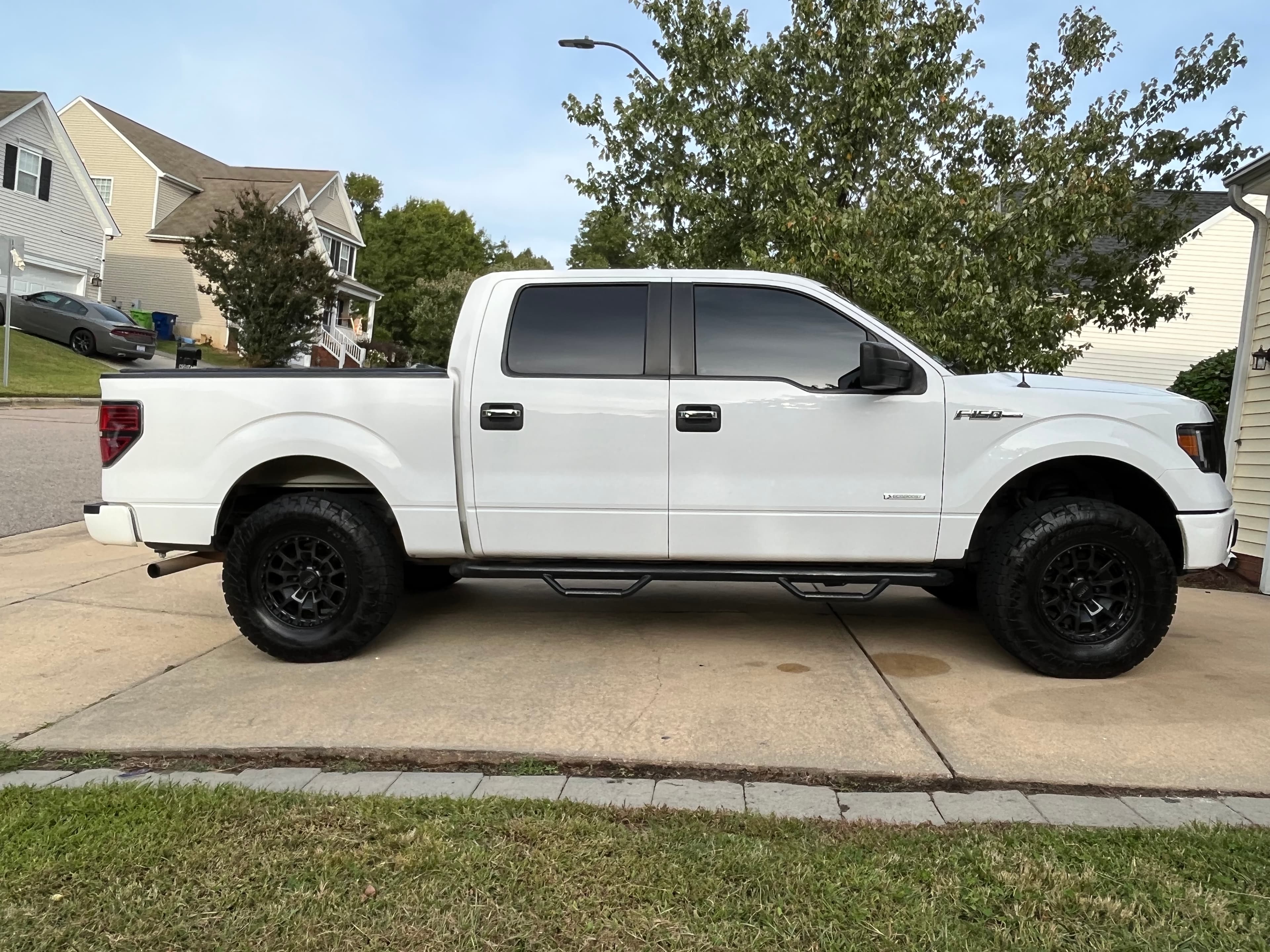 White Ford F-150 pickup truck with tinted windows and black wheels on a driveway.